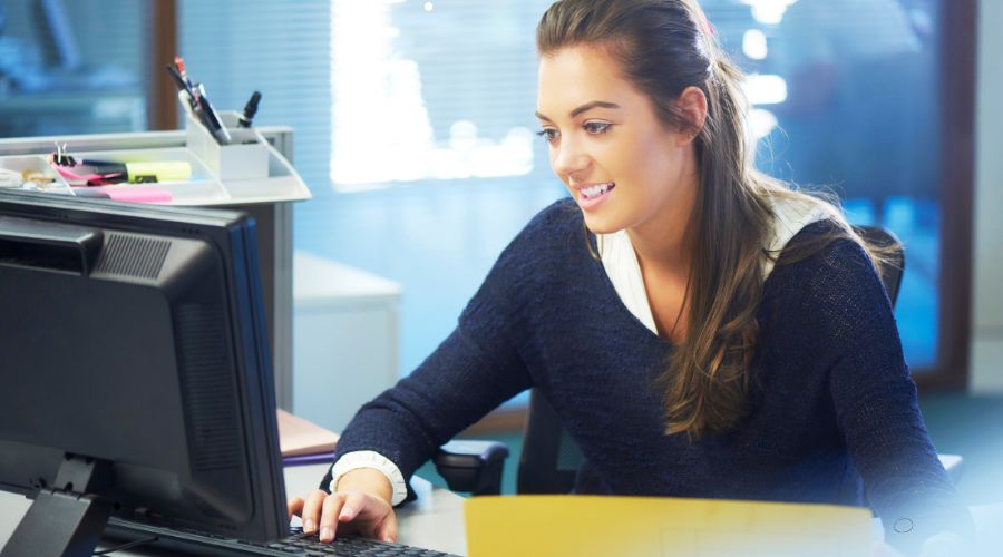 Image showing a customer service representative that is at her computer smiling to help customers learn time and attendance software with free phone and email support